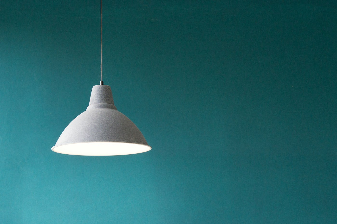 A simple metal pendant light against a green wall